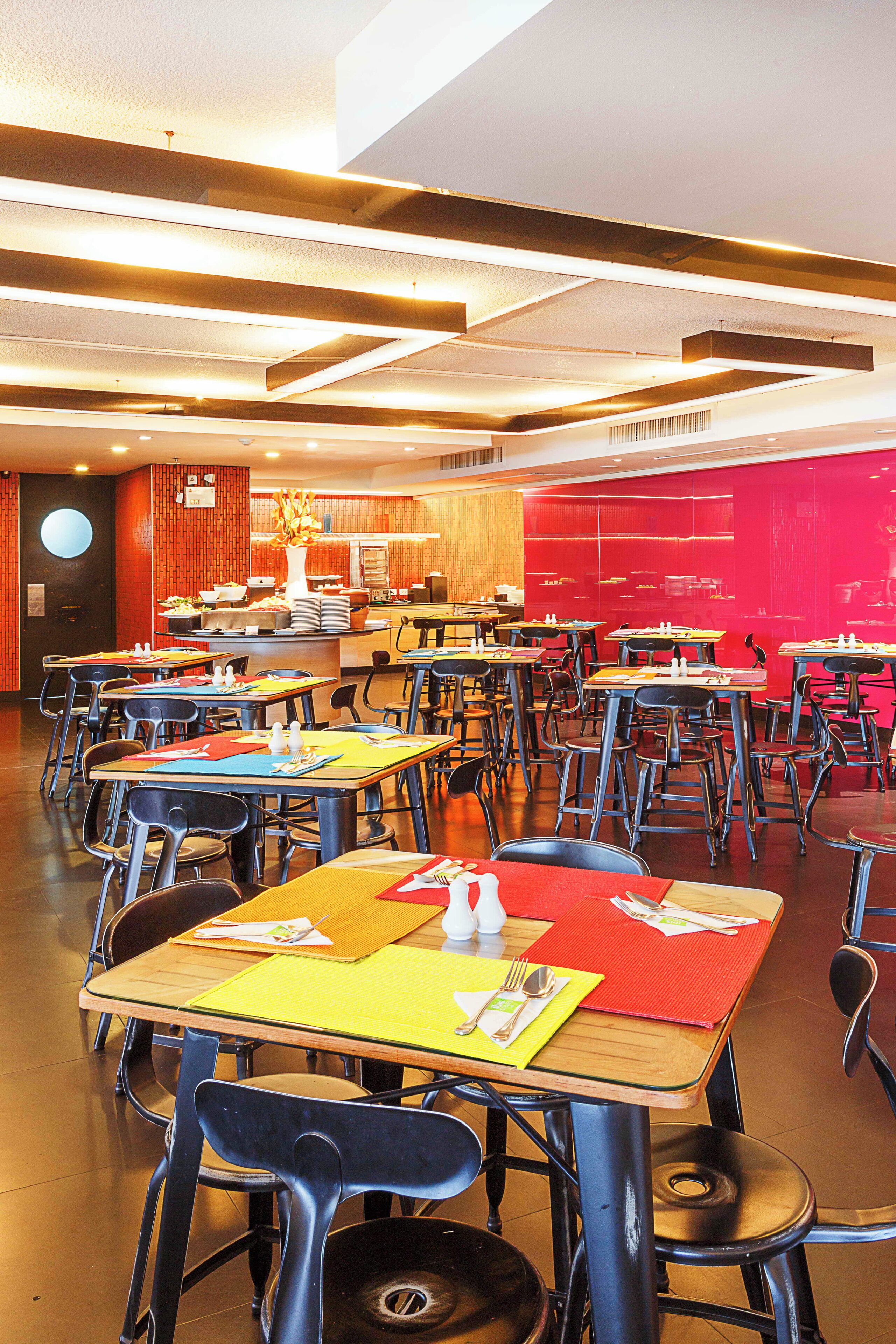 Un comedor amplio con varias mesas y sillas, una barra central y una pared de acento rojo brillante.