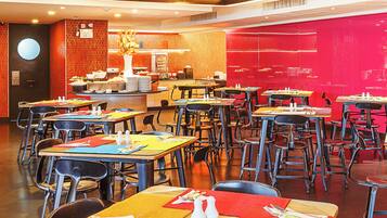 A spacious dining area with multiple tables and chairs, a central counter, and a bright red accent wall.