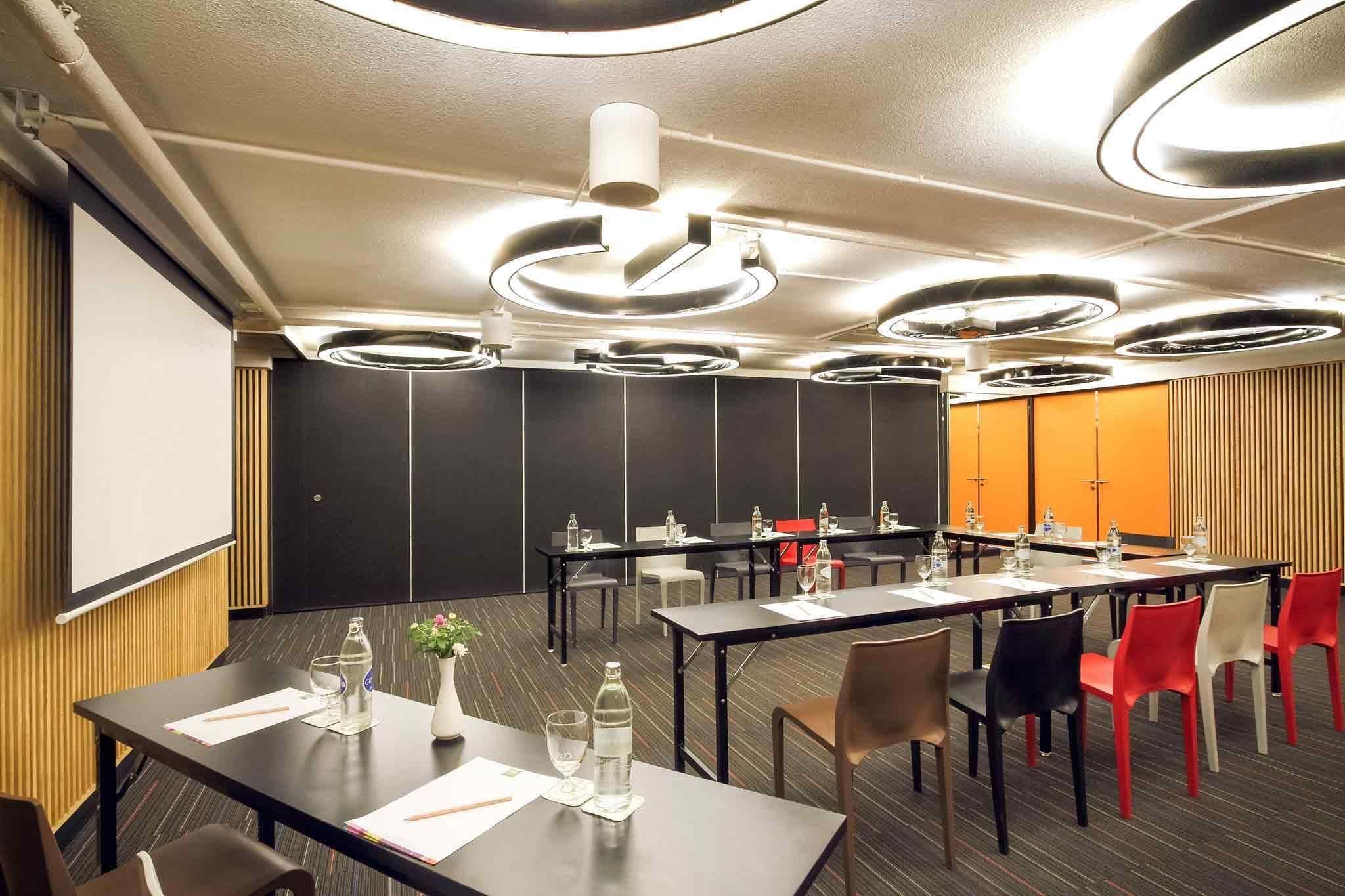 A conference room with tables, chairs, a projector screen, and a large blackboard.