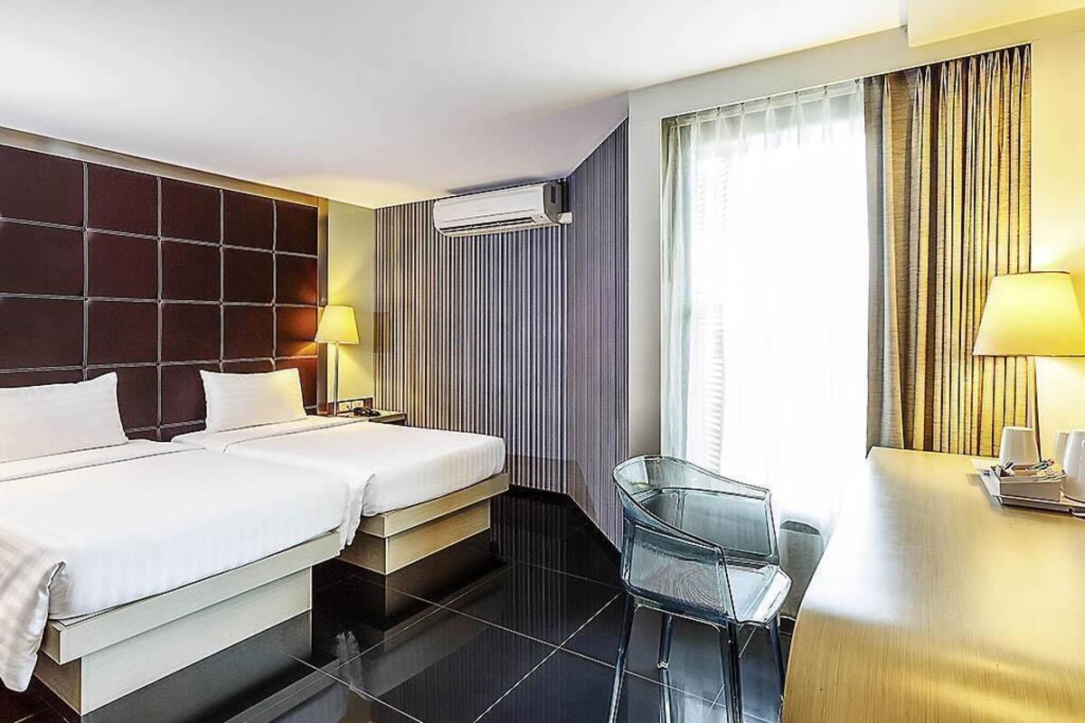Une chambre d’hôtel avec deux lits, un bureau, une chaise, une fenêtre avec des rideaux et un appareil de climatisation.