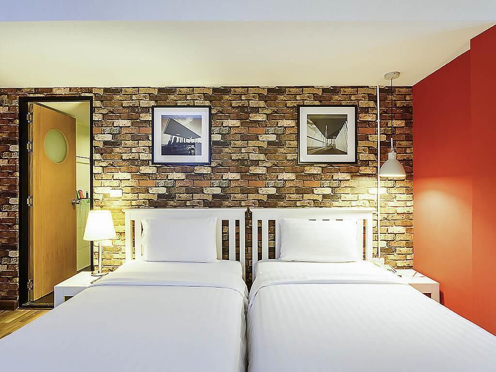 A hotel room with two beds, a brick wall, and framed pictures.