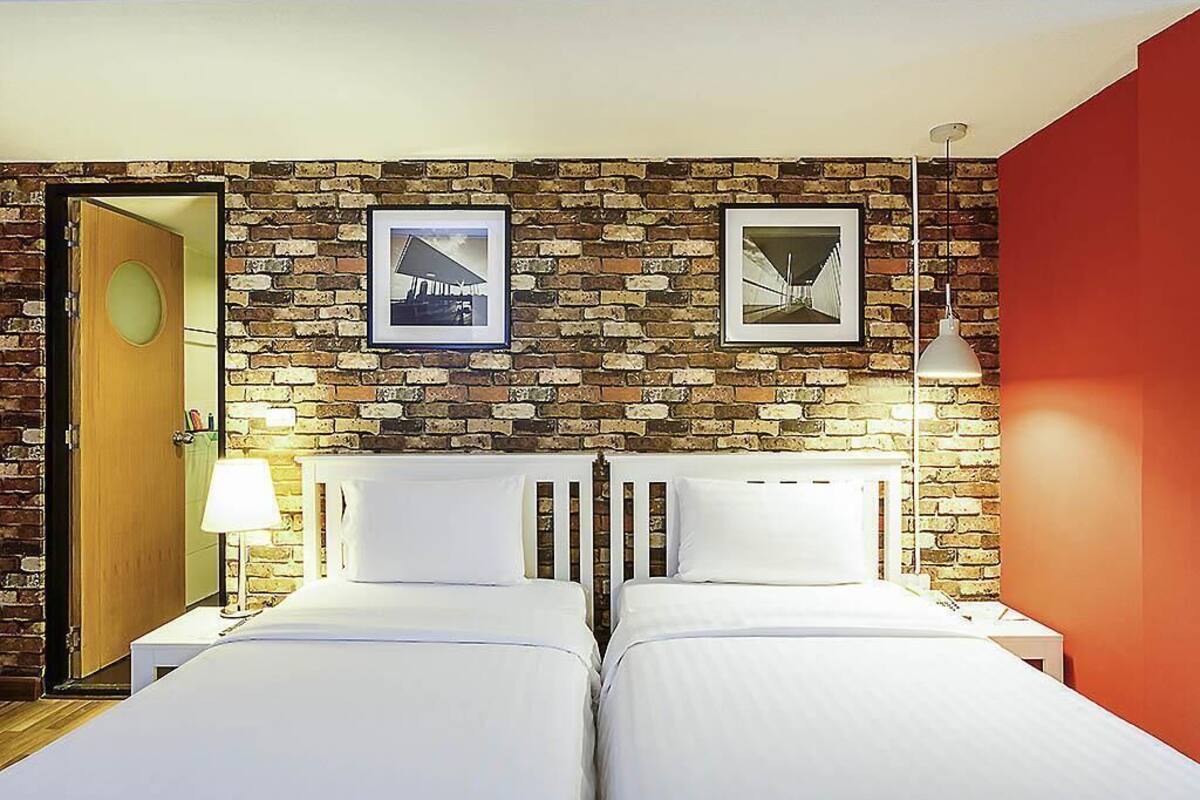 A hotel room with two beds, a brick wall, and framed pictures.
