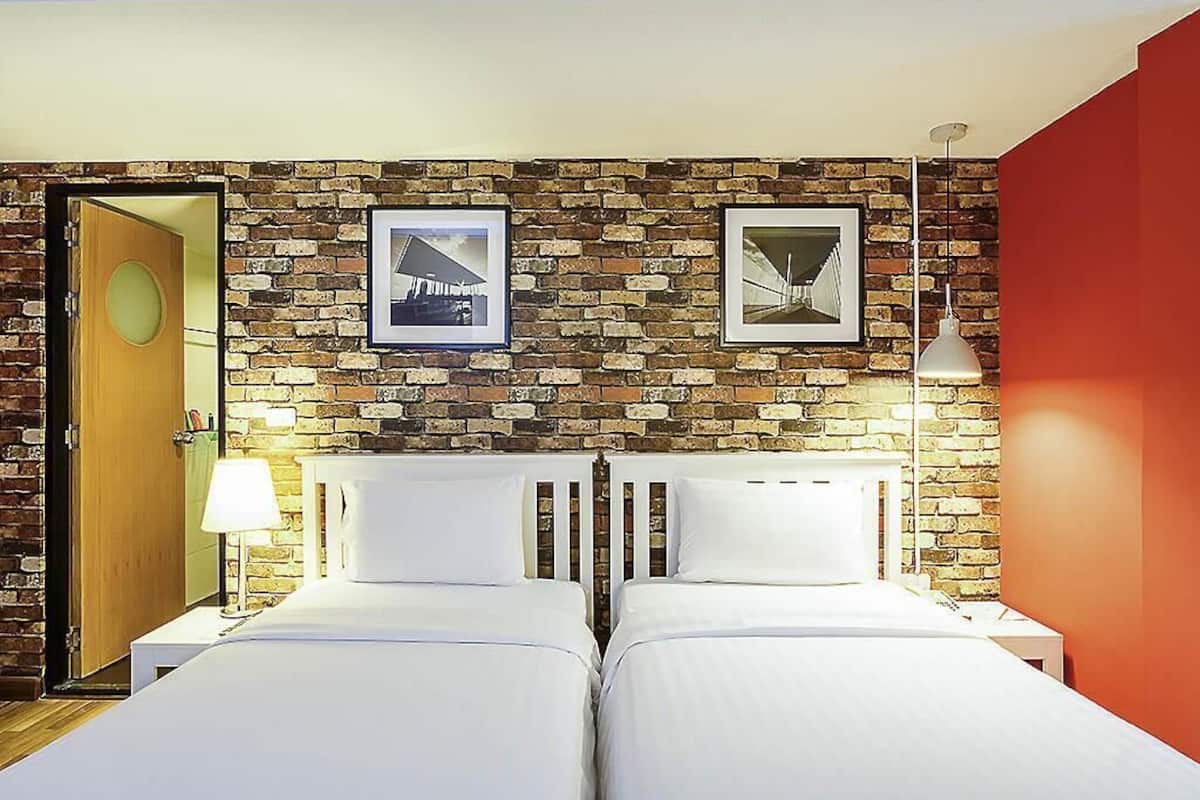 A hotel room with two beds, a brick wall, and framed pictures.