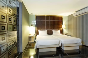 A hotel room with two beds, a large padded headboard, a modern lamp, and a wall-mounted air conditioner. - ibis Styles Chiang Mai (Chiang Mai)