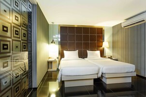A hotel room with two beds, a large padded headboard, a modern lamp, and a wall-mounted air conditioner.