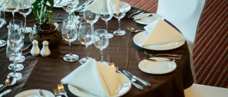 Una mesa de comedor lista para una comida, con sillas blancas, un florero con flores y vistas al exterior a través de amplias ventanas.