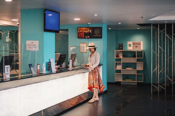 Un mostrador de recepción con una pantalla digital, un cartel que indica la disponibilidad de WiFi y un letrero para la sala de té.