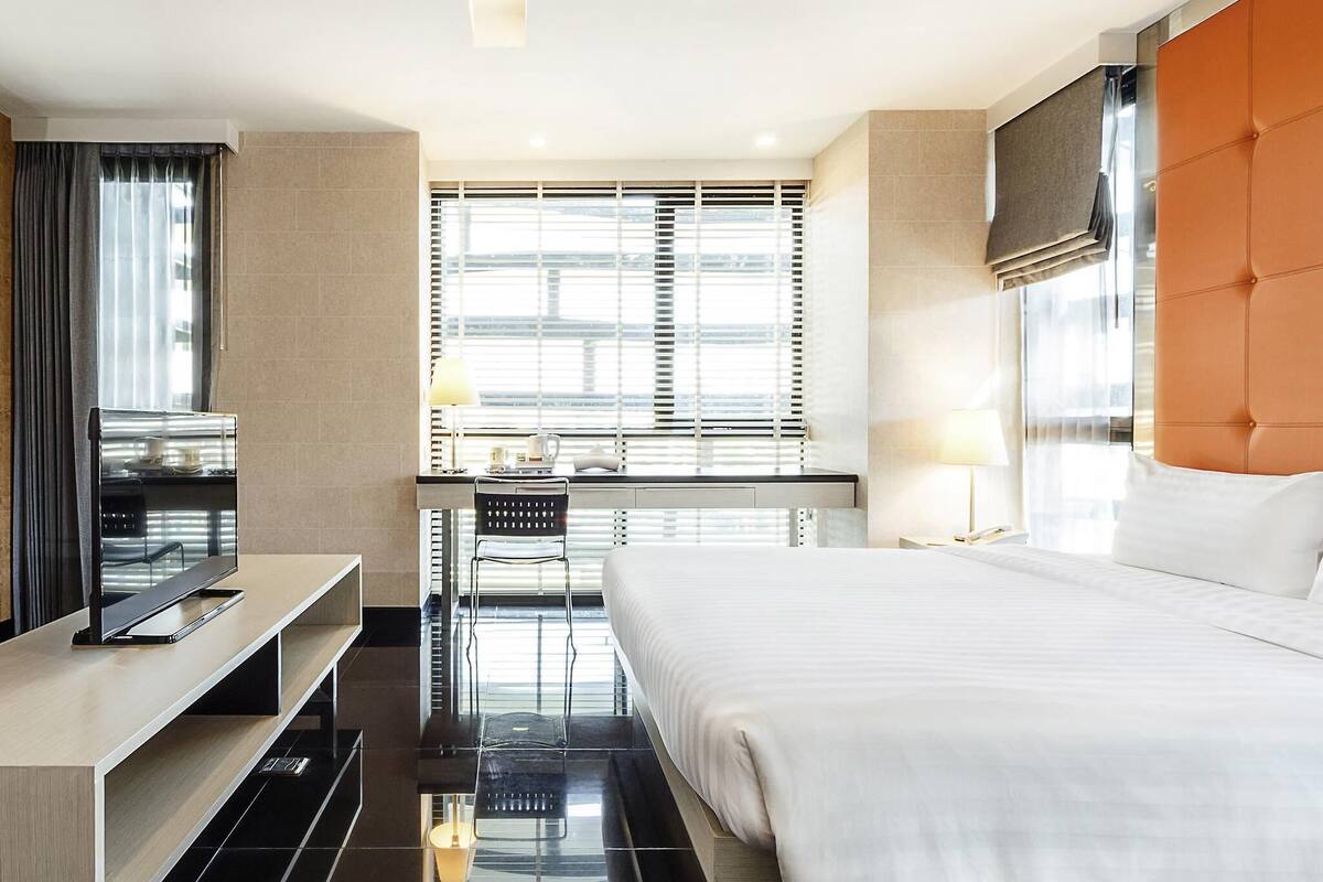 Une chambre d’hôtel équipée d’un lit, d’un bureau, d’une chaise, d’une télévision et d’une fenêtre avec des stores.