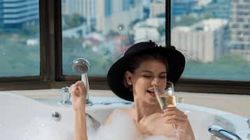 A person in a bathtub with a cityscape view through large windows.