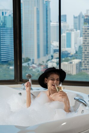 A person in a bathtub with a cityscape view through large windows. - Hotel Muse Bangkok, Autograph Collection (Bangkok)