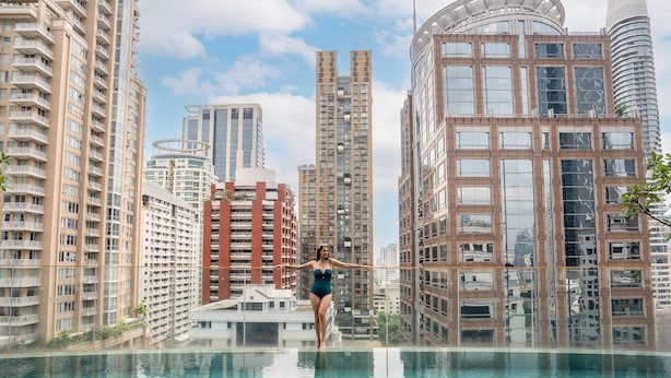 Eine Frau steht an einem Pool auf einem Dach mit Stadtblick im Hintergrund.