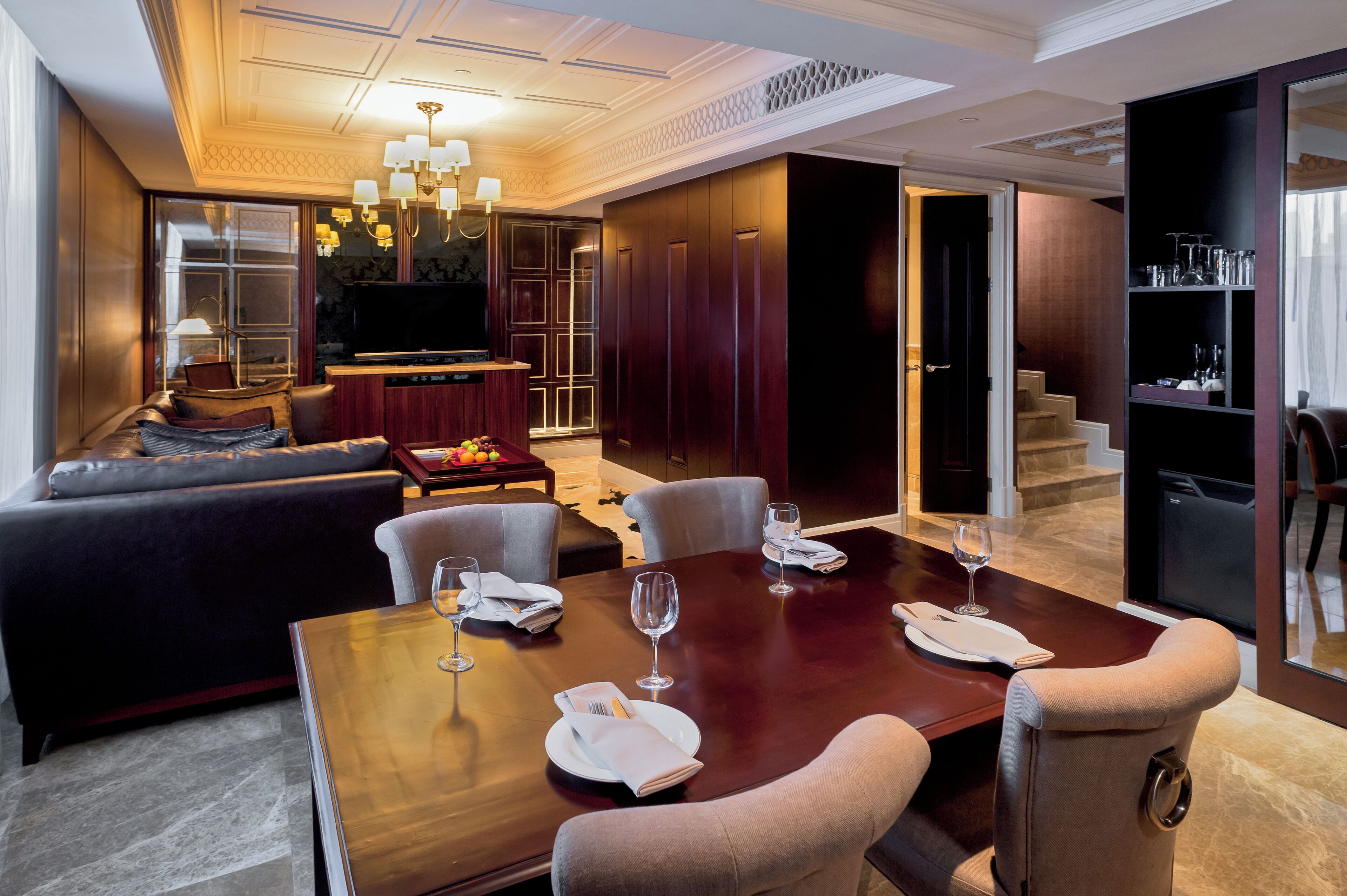 A modern hotel room with a dining area, a sofa, a TV, and a bookshelf.