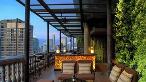 Eine Dachterrasse mit Blick auf die Stadtlandschaft, mit einer Bar und Hockern sowie einer Lounge mit Sofa und Tisch.