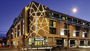 Un hotel moderno con un diseño de iluminación geométrica en la fachada, una entrada despejada y un letrero visible que dice "NOVOTEL".
