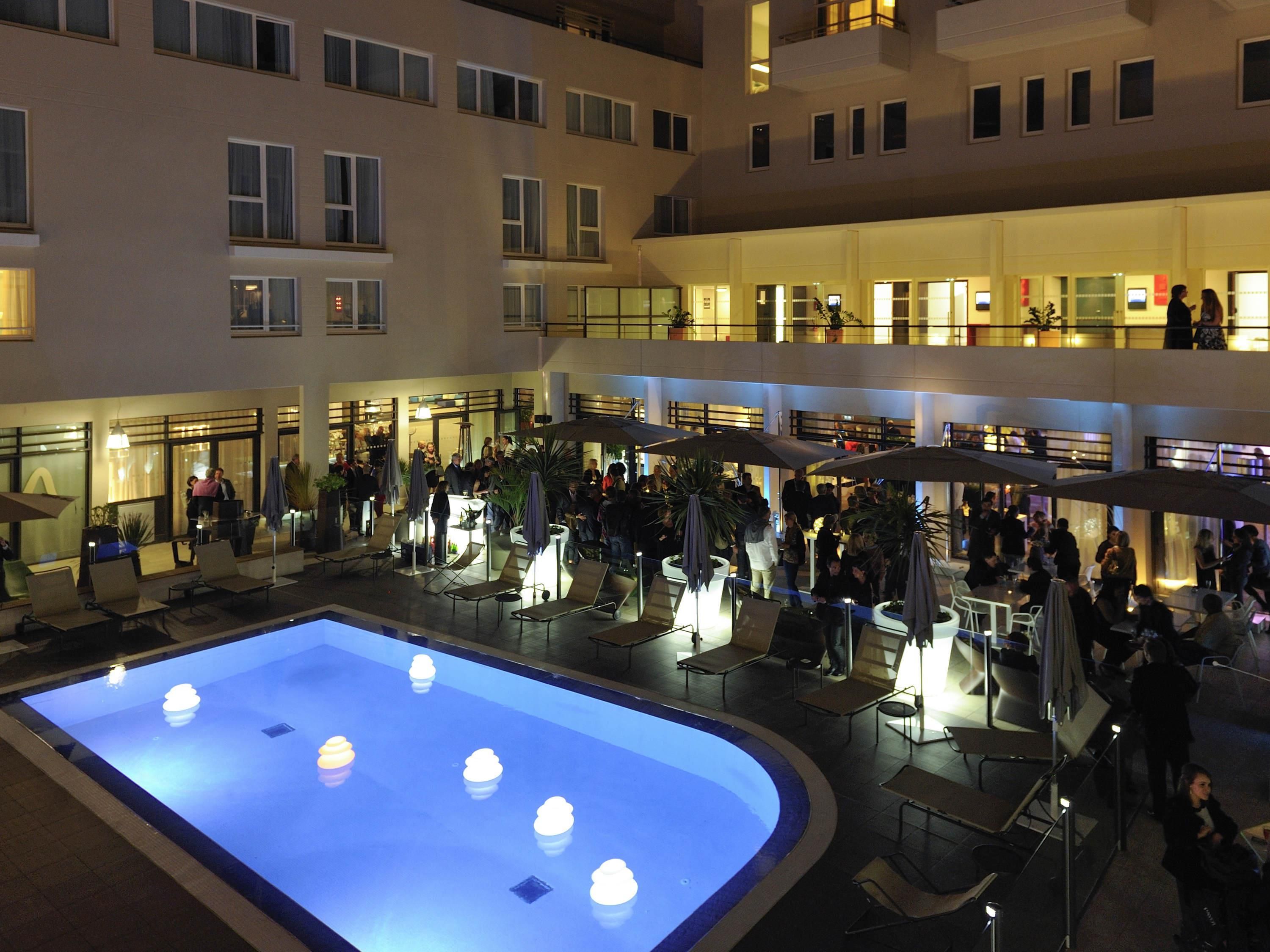 Un vestíbulo de hotel con varios niveles, un área de piscina central, asientos al aire libre y múltiples pisos con ventanas y balcones visibles.