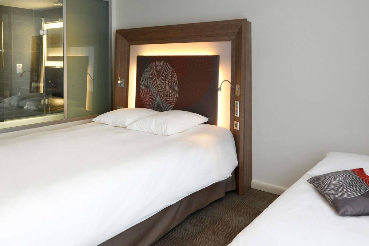 Ett hotellrum med en säng, en stor spegel och ett unikt konstverk på väggen.