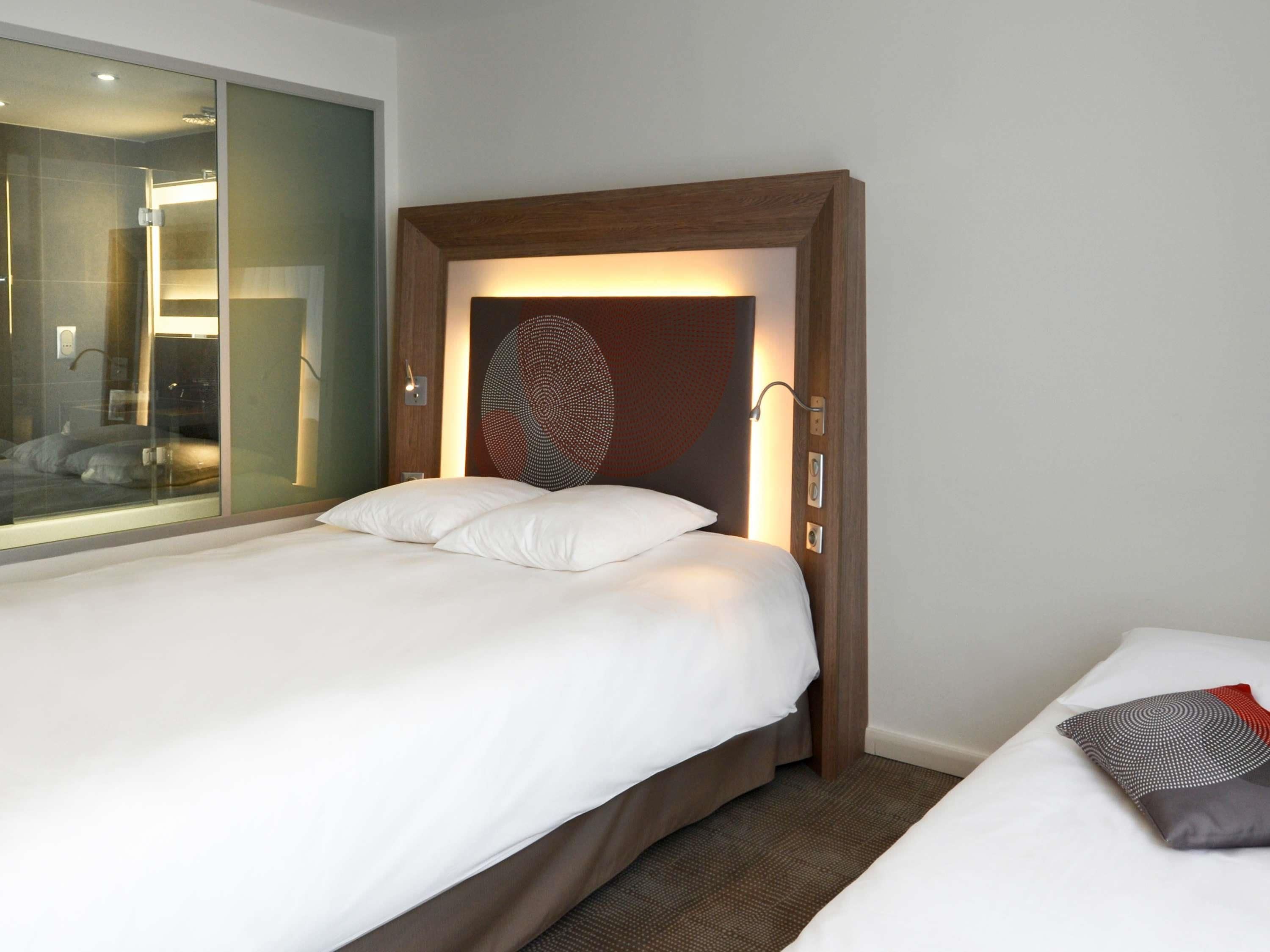 A hotel room with a bed, a large mirror, and a unique wall art piece.