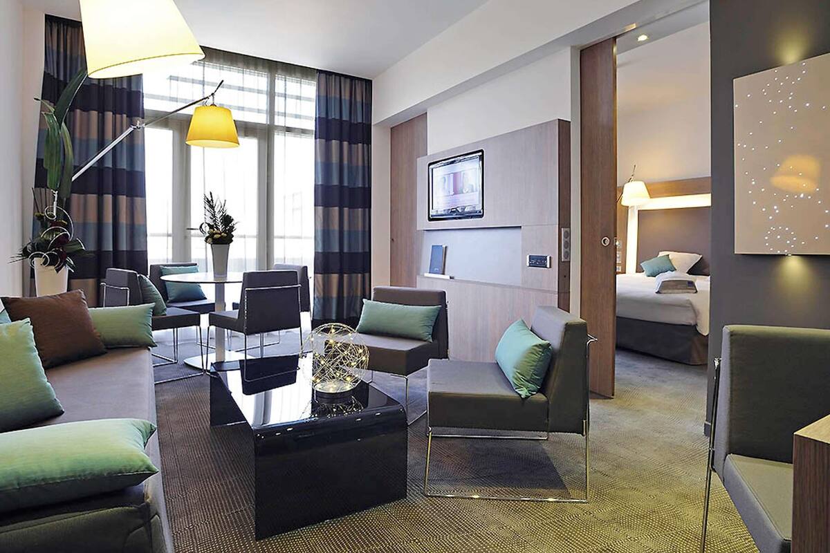 Ett modernt hotellrum med en soffa, fåtöljer, ett soffbord, en tv, ett skrivbord och en säng.