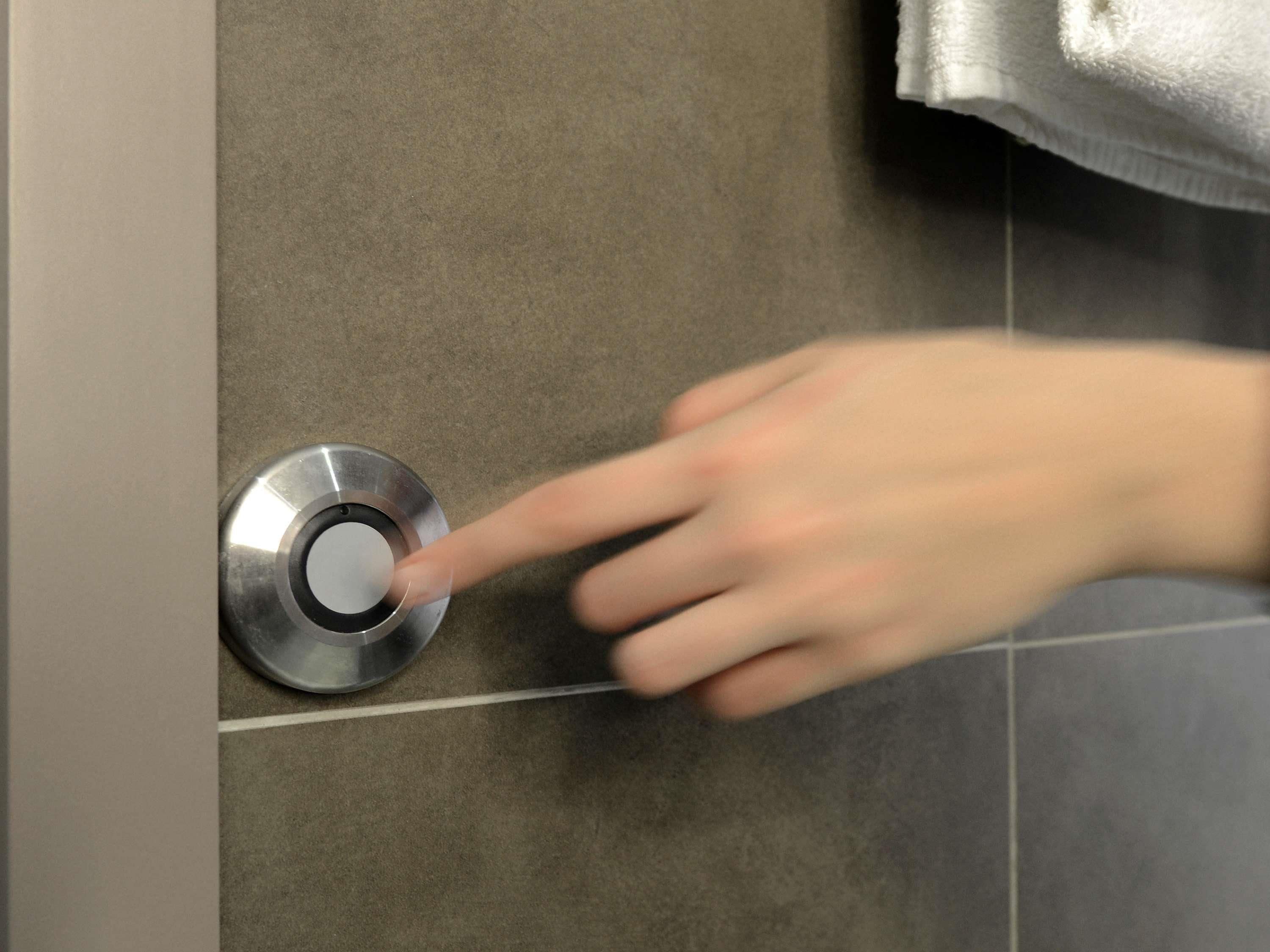 A hand pressing a metallic door handle on a tiled wall.