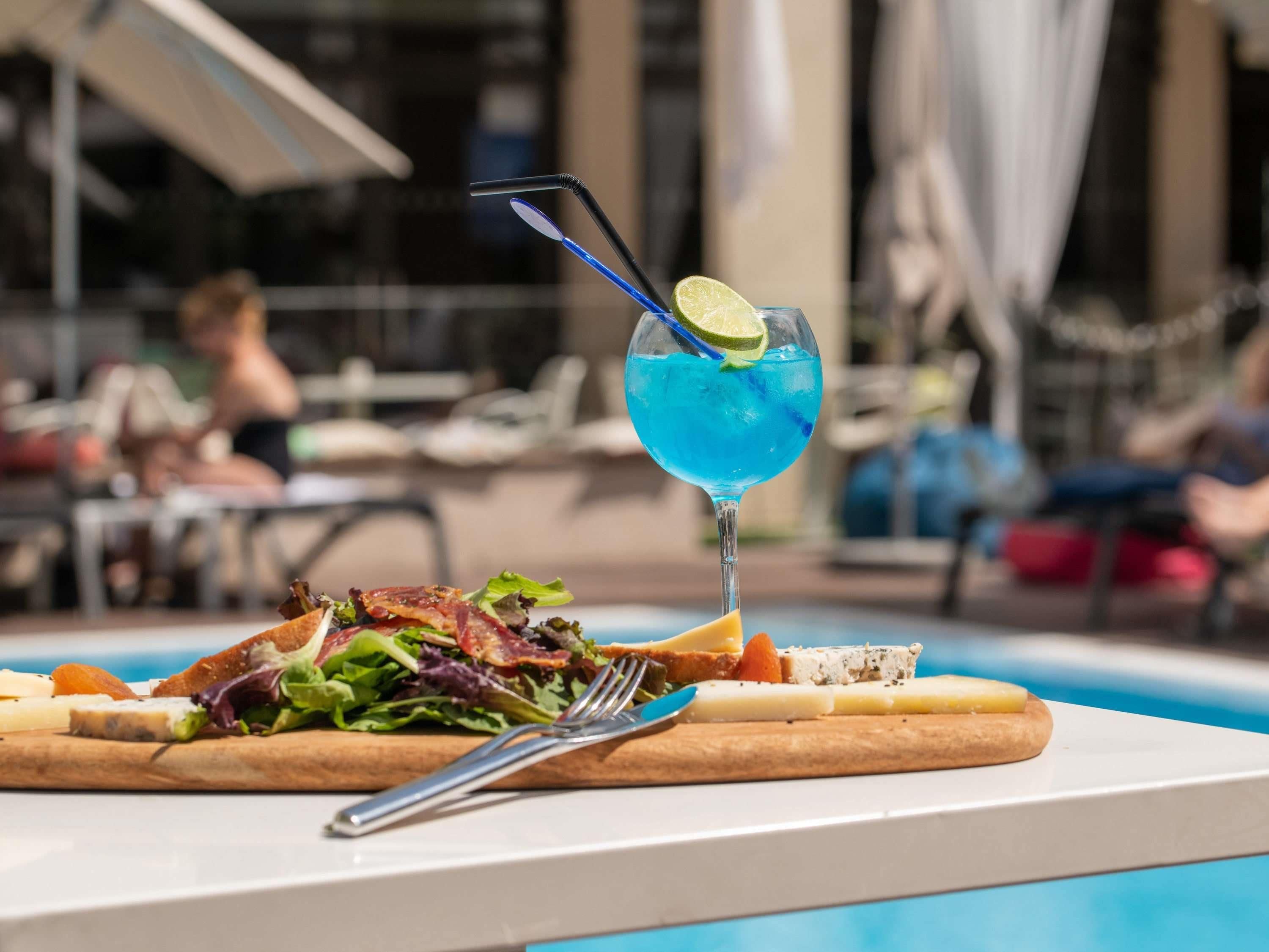 A dining table with a salad and a blue cocktail with a lime garnish.