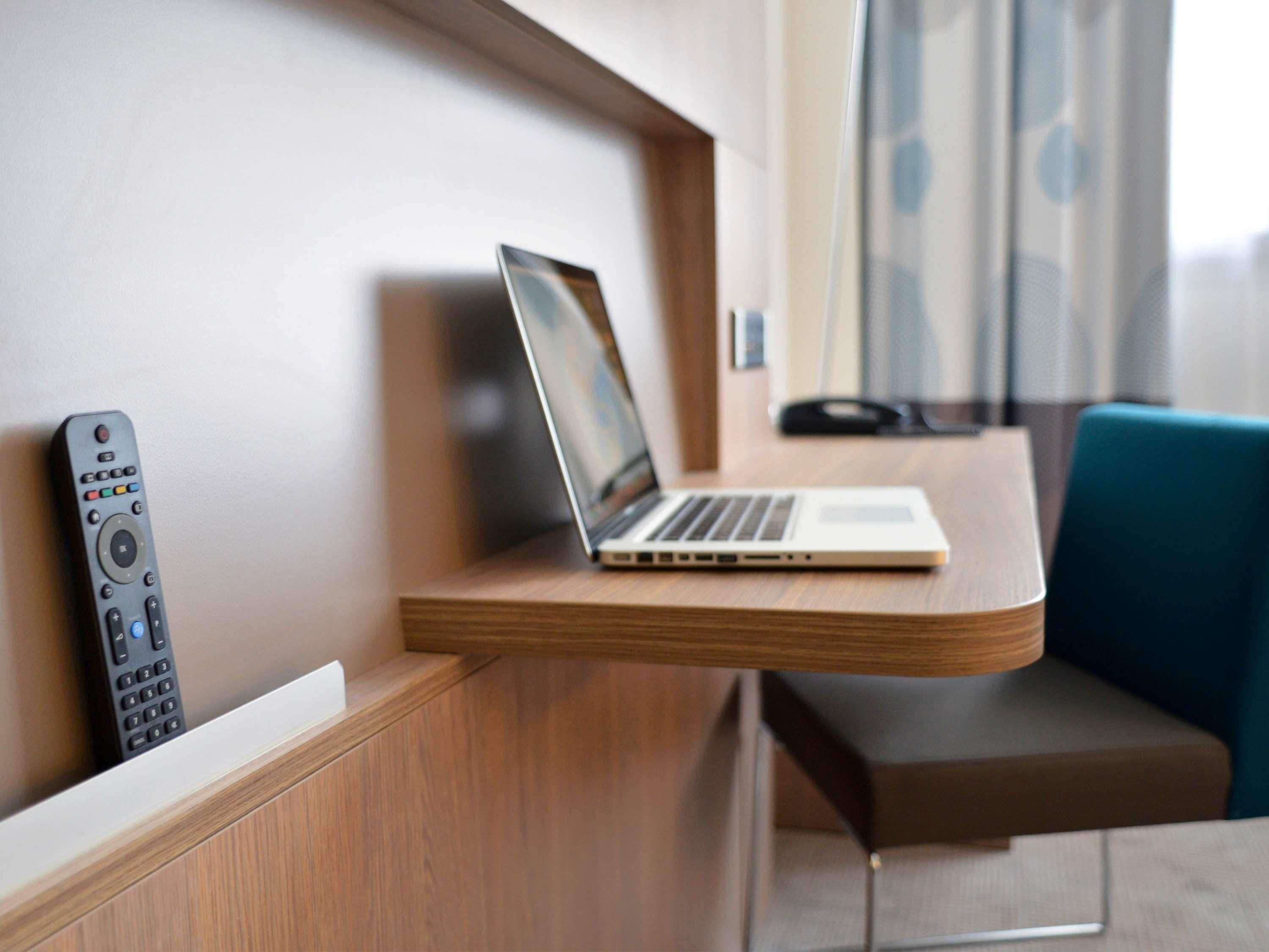 A laptop on a wooden desk with a remote control on the left.