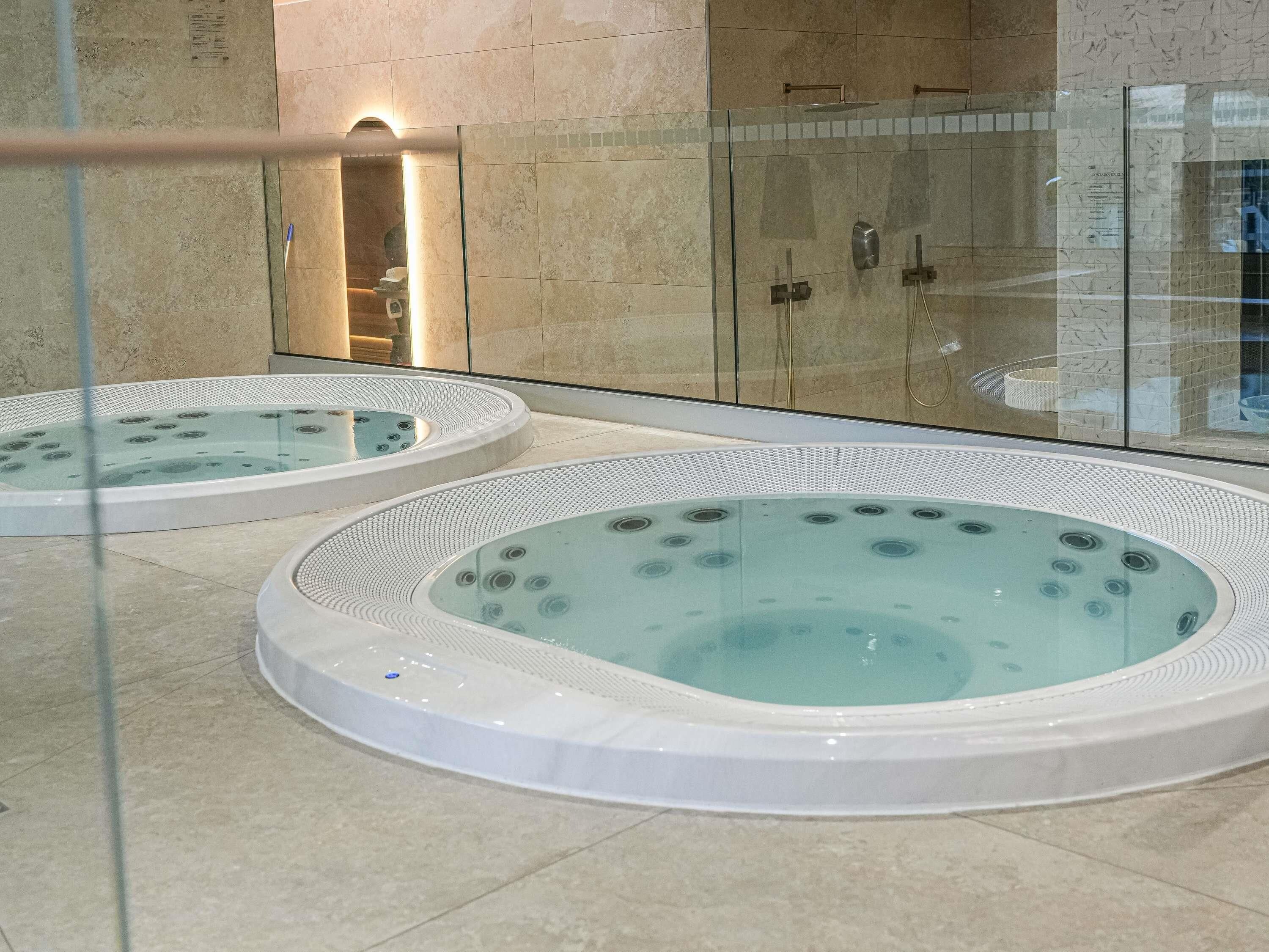 Un área de spa con dos jacuzzis y una zona de ducha con paredes de cristal.