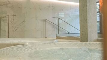 Un área de spa con paredes de mármol, una bañera de hidromasaje y una escalera.