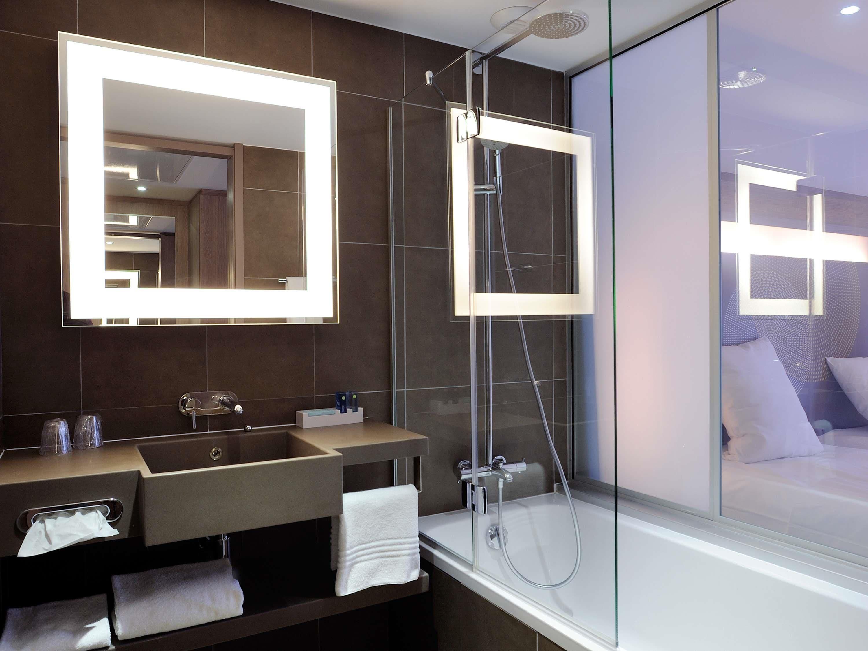 Un baño moderno con un espejo grande, una ducha con cerramiento de vidrio y un lavamanos con toalla.