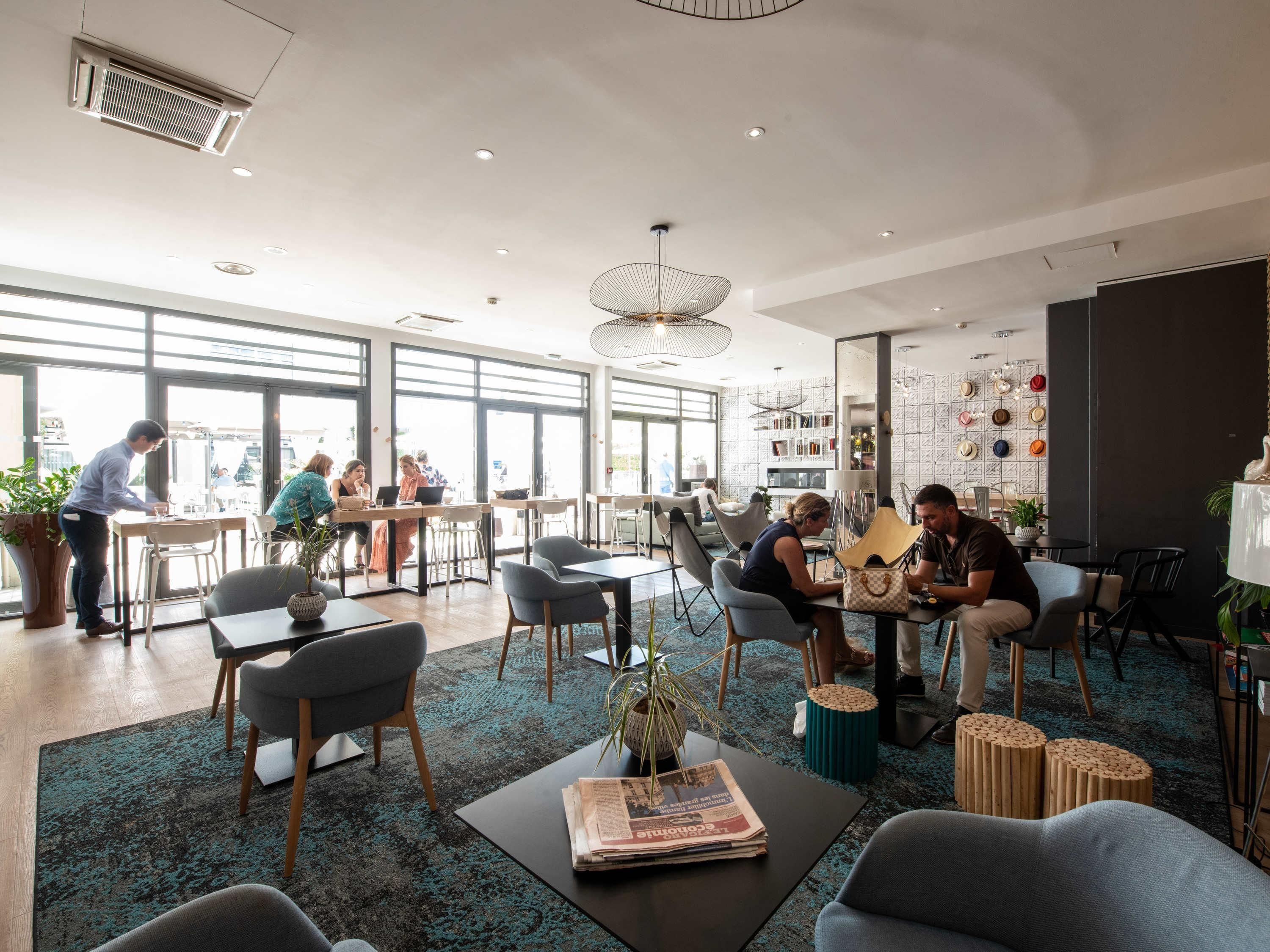 Un intérieur moderne avec de grandes fenêtres, un espace salon central et une variété de tables et de chaises.