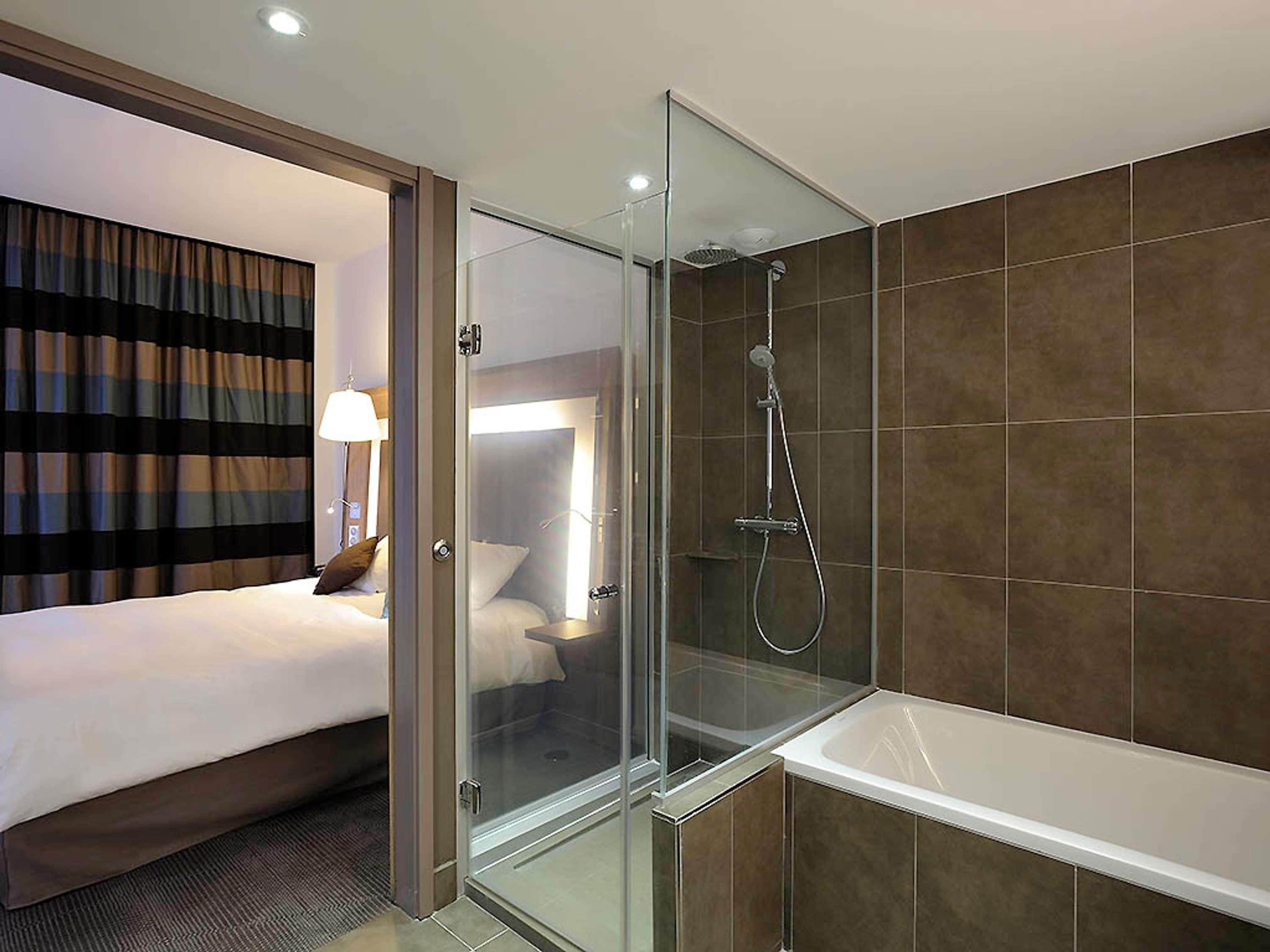 Une chambre d’hôtel dotée d’une douche en verre, d’un grand lit et d’une salle de bain séparée avec une baignoire.