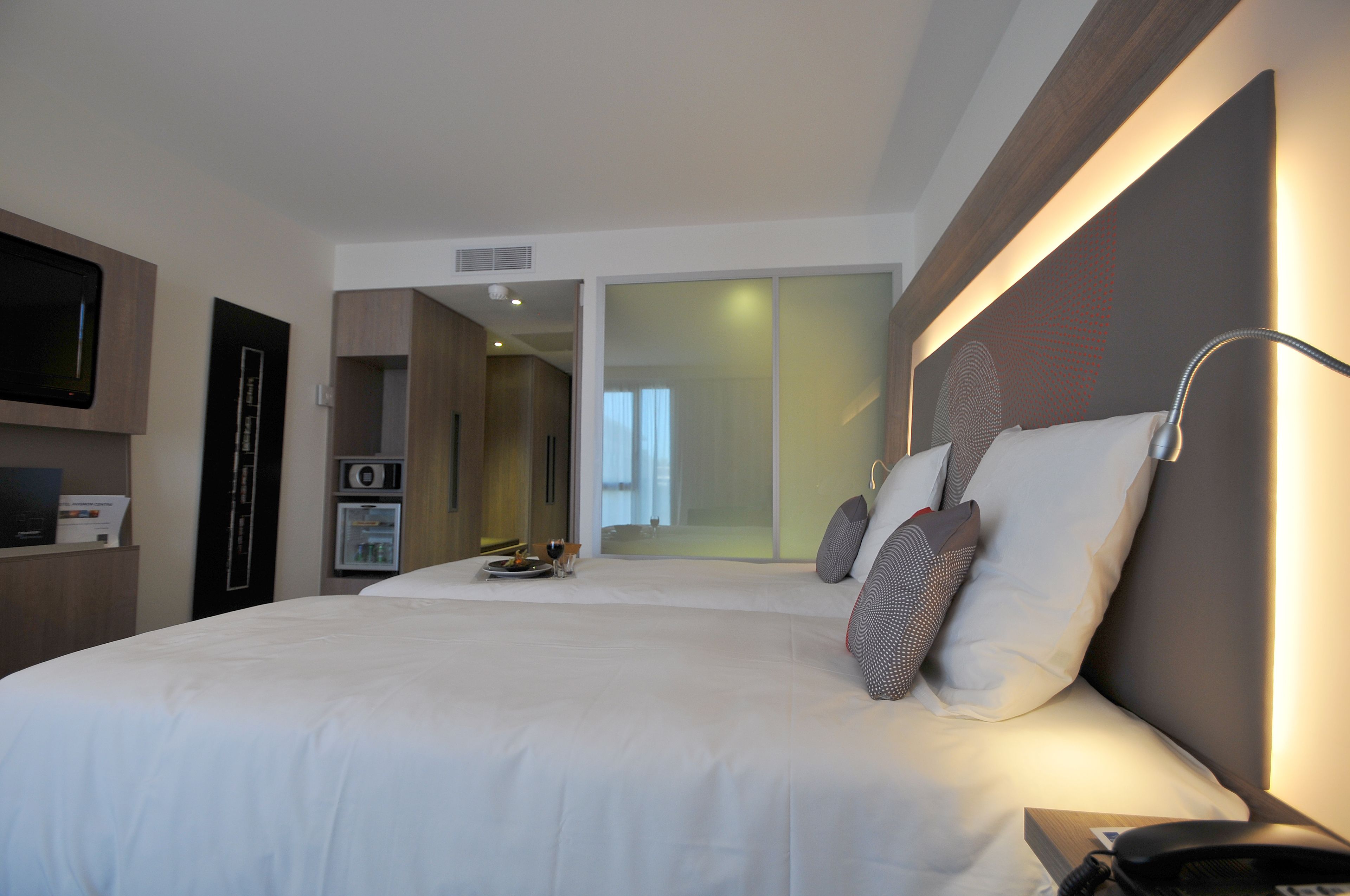 A modern hotel room with a large bed, bedside table, and a flat-screen TV mounted on the wall.
