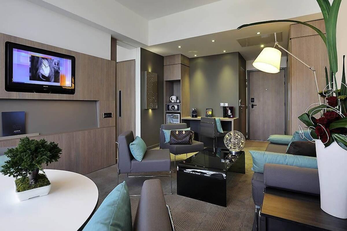A modern living room with a flat-screen TV, sofas, a coffee table, and a potted plant.