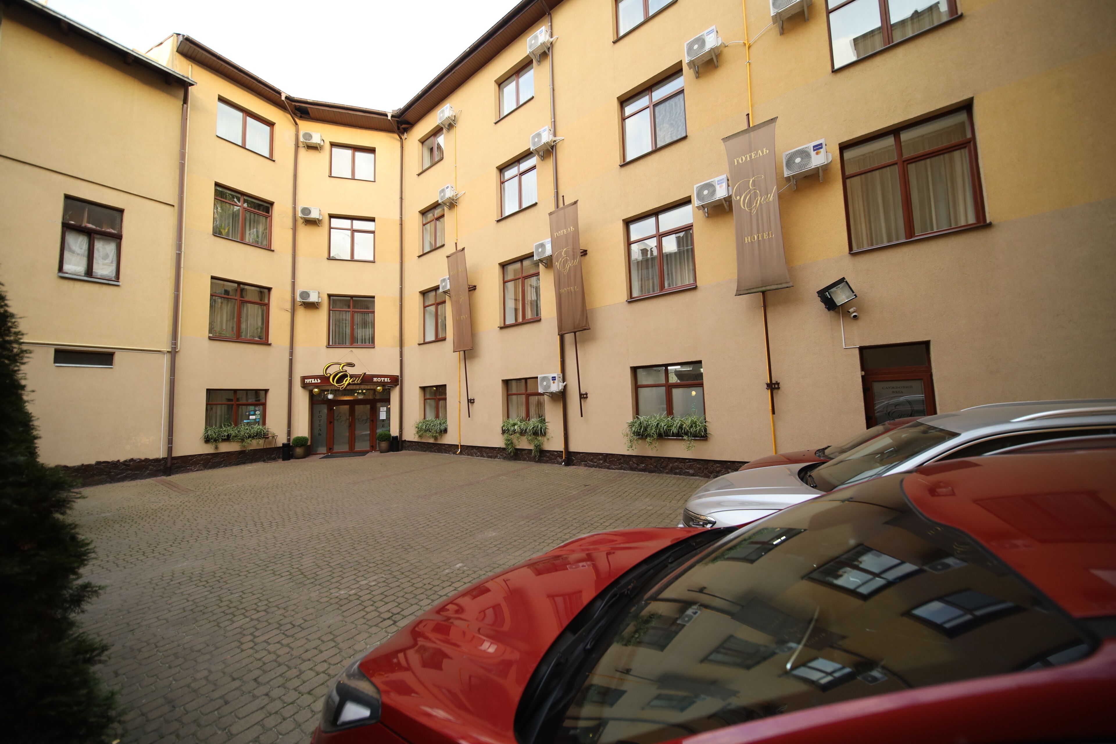 A hotel with a yellow facade, multiple windows, and a paved courtyard.