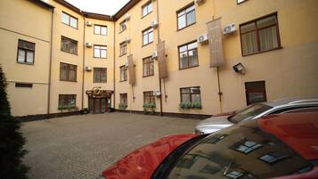 A hotel with a yellow facade, multiple windows, and a paved courtyard.
