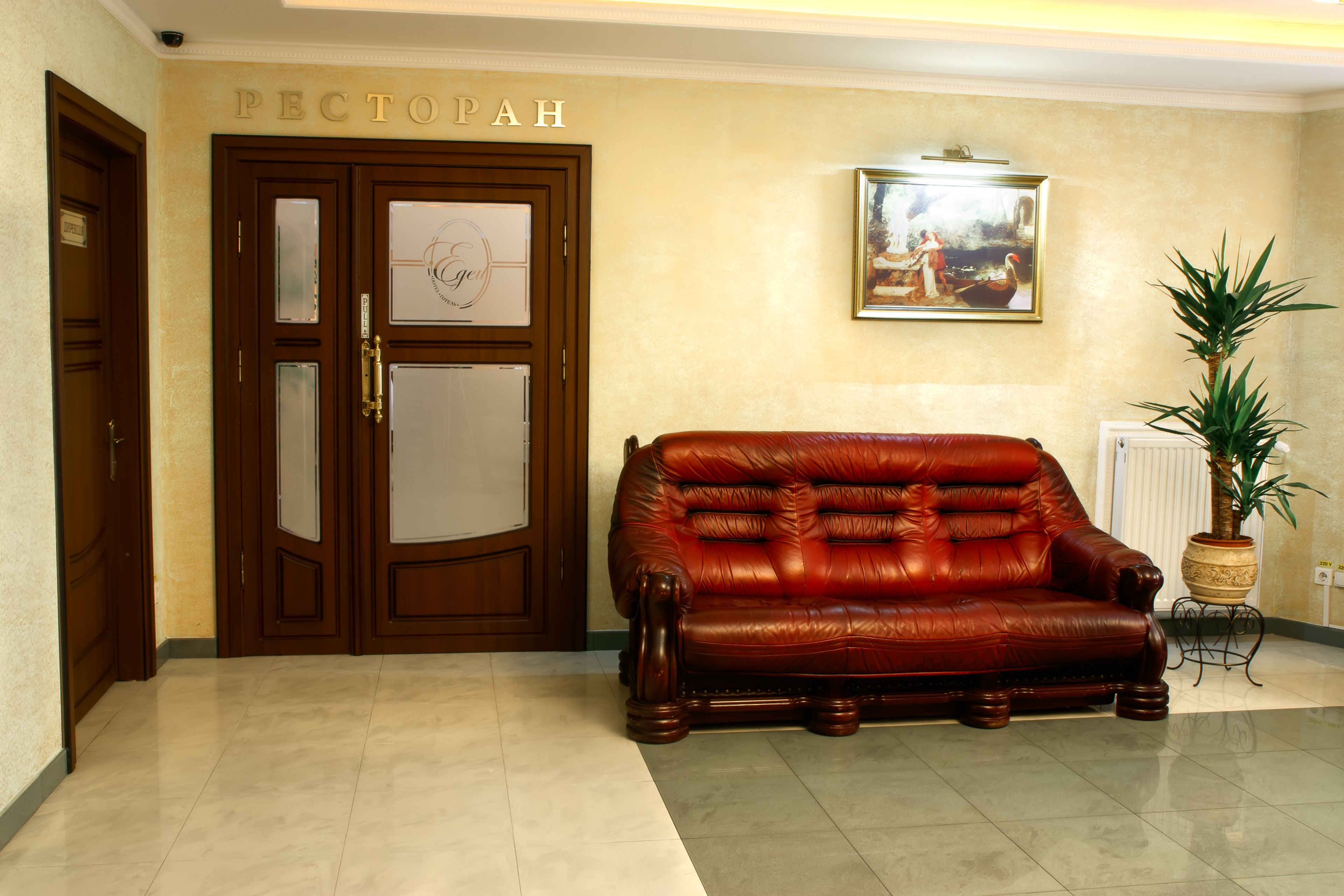 A lobby with a wooden door labeled "PECTOPAH," a red leather sofa, a framed painting, and a potted plant.