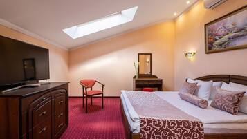 A hotel room with a bed, a desk, a chair, a TV, a dresser, a mirror, and a painting on the wall.