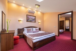 Habitación de hotel con una cama grande, una mesita de noche de madera, un banco tapizado rojo, un aire acondicionado de pared, un cuadro y un espejo.