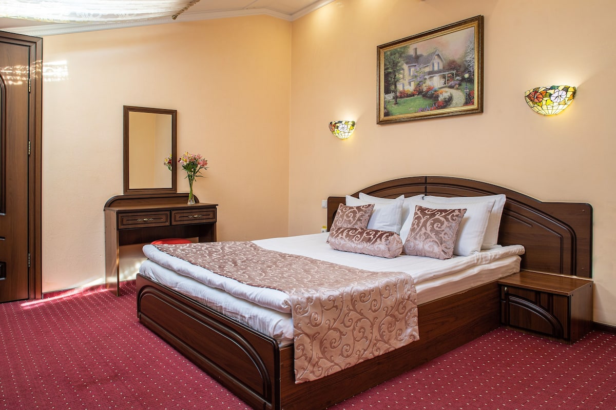 A neatly made bed with a patterned bedspread, a bedside table with a lamp, a dresser, and a mirror.