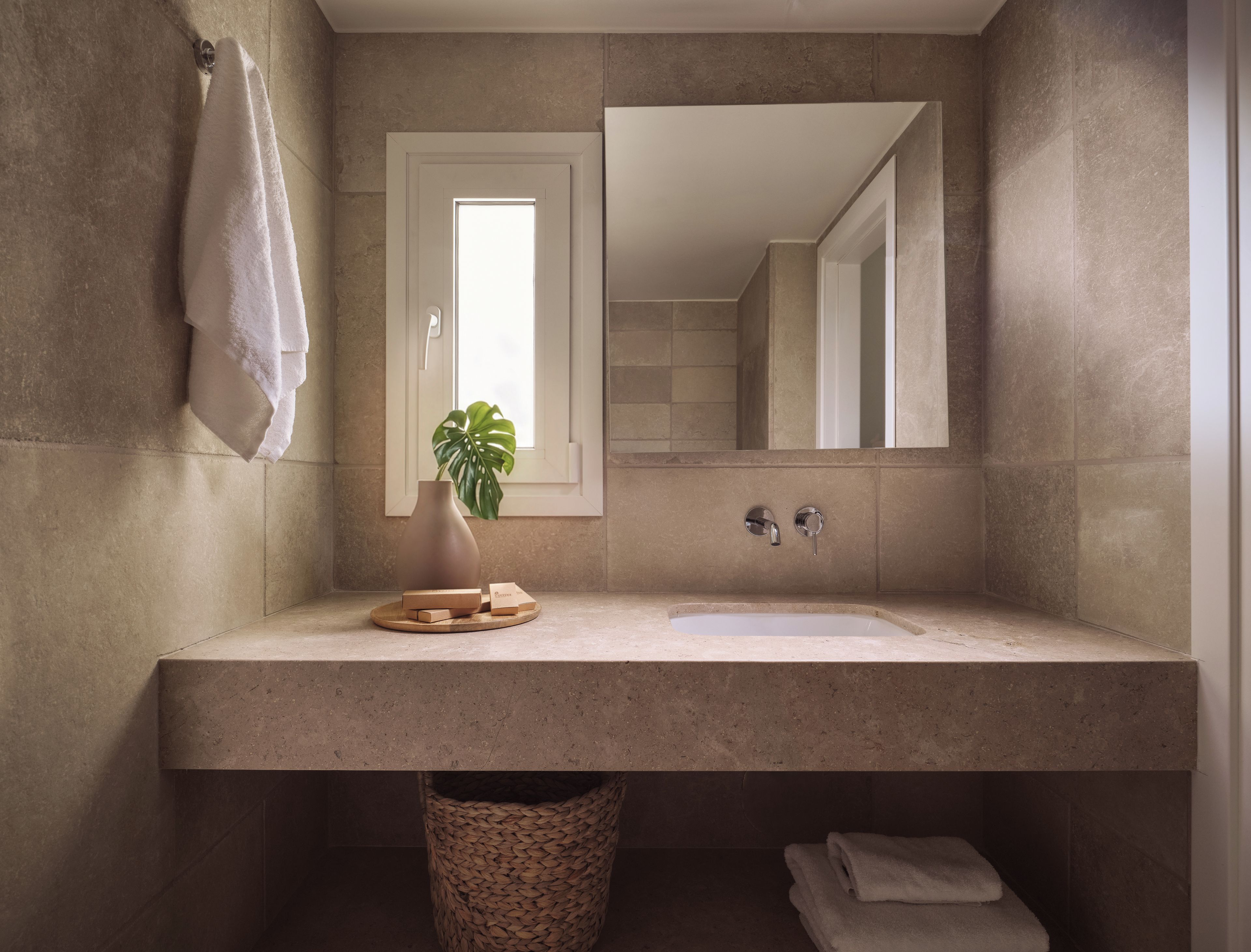 A bathroom with a large mirror, a sink, a towel rack, a plant, and a trash bin.