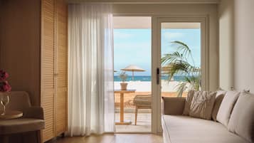Una habitación con sofá, una mesa con un vaso y vista a una playa a través de un ventanal.