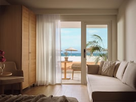 Una habitación con sofá, una mesa con un vaso y vista a una playa a través de un ventanal.