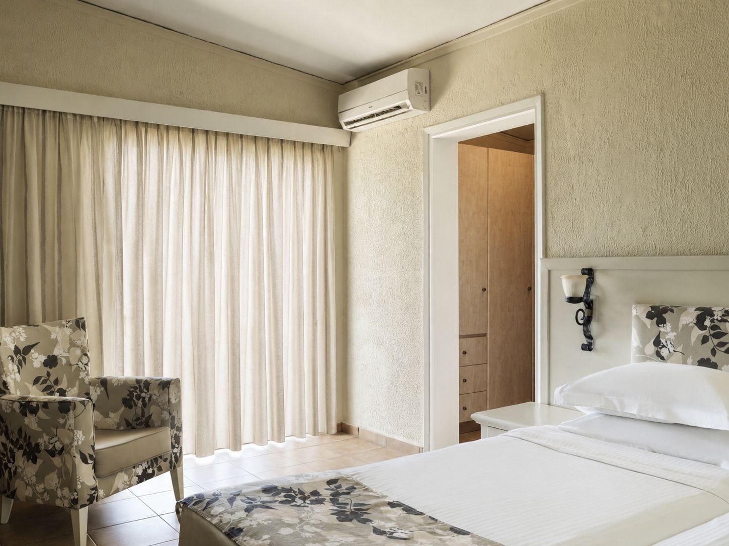 Quarto de hotel com cama, poltrona, guarda-roupa e ar condicionado.