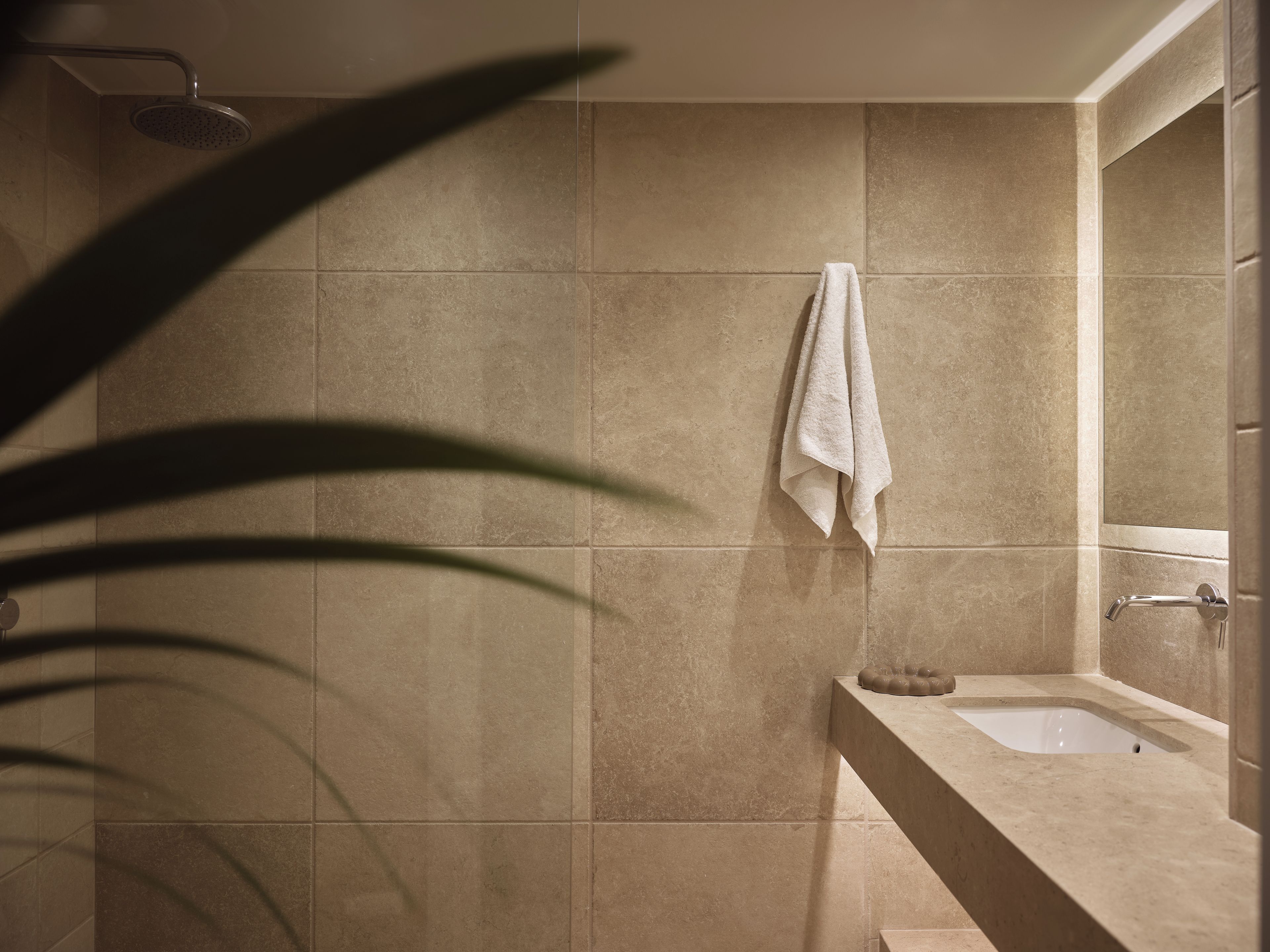 Un baño con baldosas color crema, una toalla blanca colgada en la pared y una bañera.