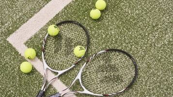 Two tennis rackets and five tennis balls on a green artificial turf surface.