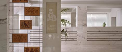 A modern interior with a tiled wall featuring decorative panels, a marble floor, and a staircase leading to a balcony with a view.