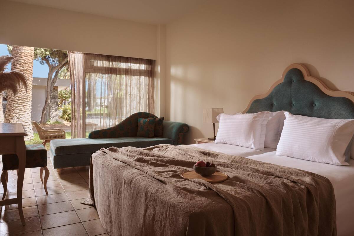 A bedroom with a bed, a chair, a table, and a view of the outdoors.