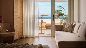 Una stanza con un divano, una sedia, un tavolo con un bicchiere e vista sulla spiaggia attraverso una porta scorrevole.
