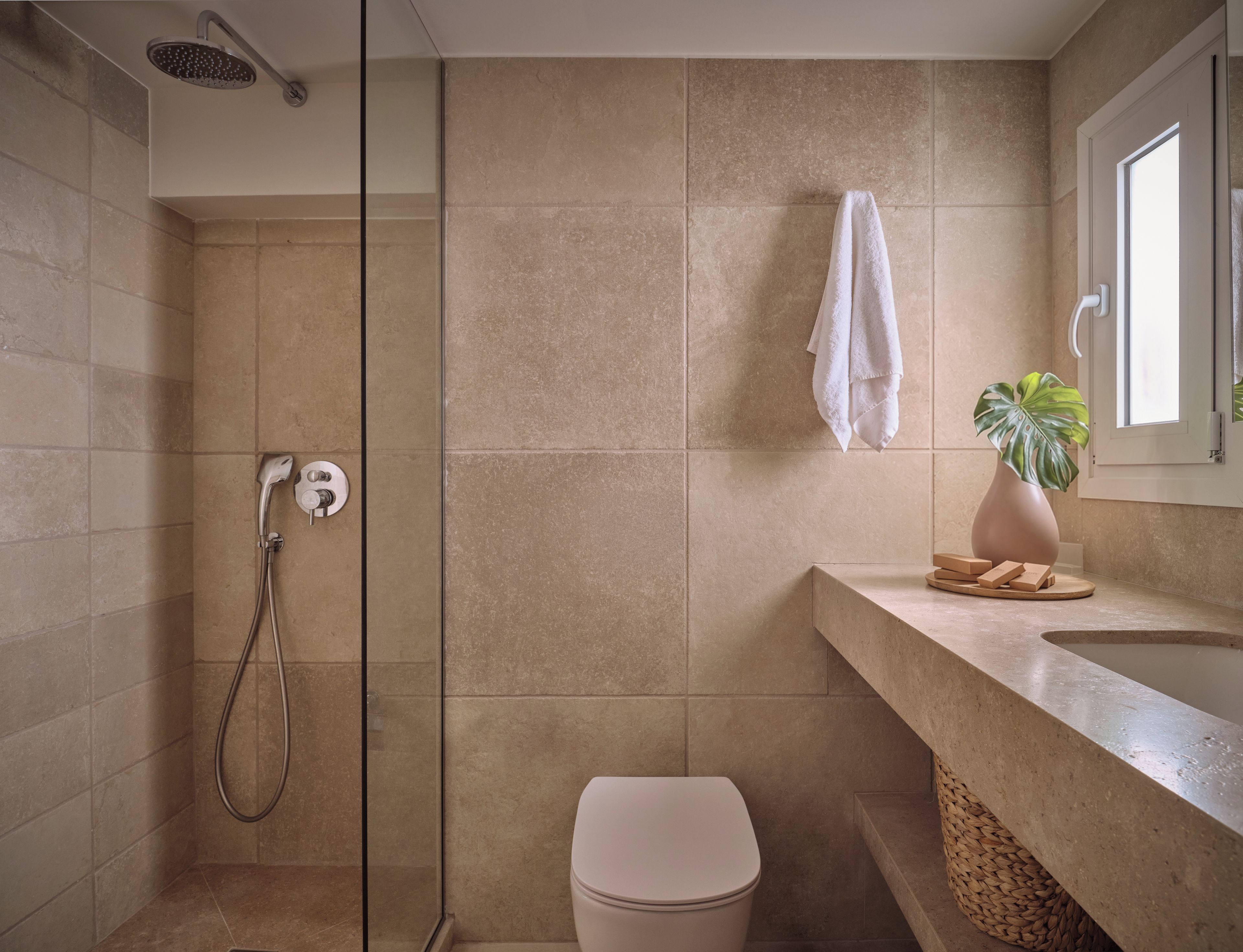 Un baño moderno con cabina de ducha de vidrio, inodoro y lavamanos con planta en maceta.