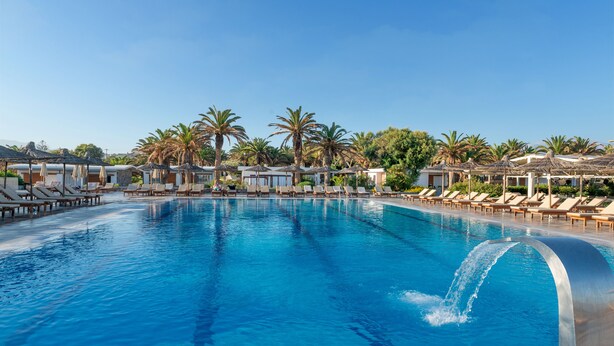 Una piscina con lettini e ombrelloni, circondata da palme e un cielo sereno.