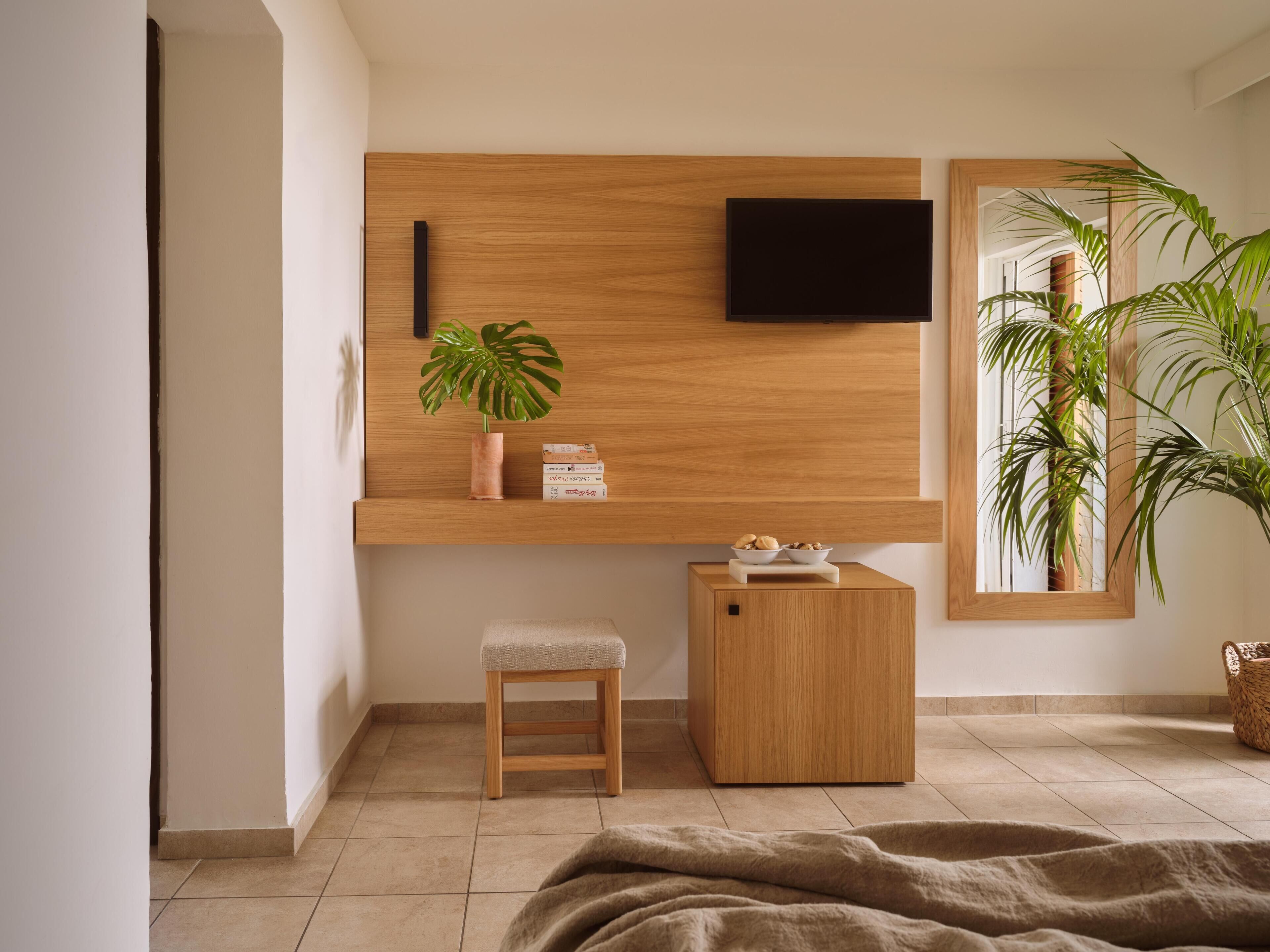 A modern room with a wooden wall unit, a flat-screen TV, a small stool, and a bench.